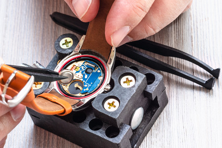 watch repairer workshop - watchmaker replaces battery in quartz wristwatch with plastic tweezers on wooden table close upの写真素材