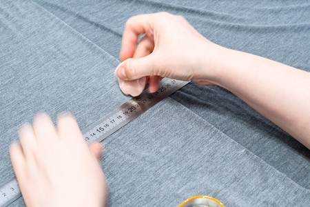 dressmaker draws pattern on gray fabric with ruler and soap on cutting table close upの写真素材