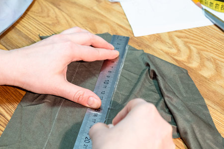 tailor draws a pattern on cloth with ruler on cutting table close up
