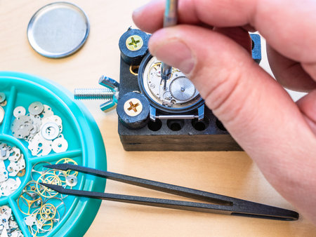 watchmaker adjusts mechanical watch by screwdriver in holder on table in workshop close up