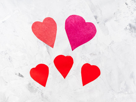 five various hearts cut from red papers on gray concrete board