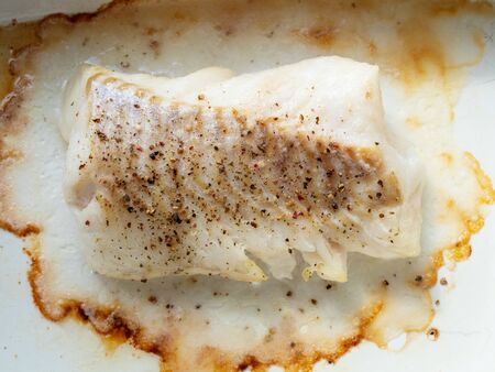 top view of piece of baked and peppered cod fish in white ceramic panの写真素材
