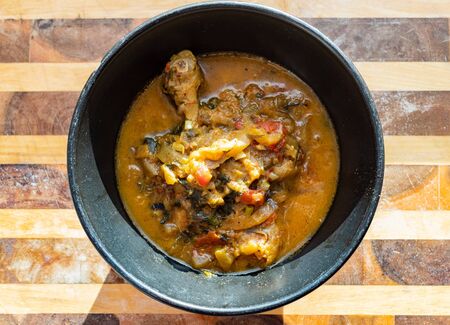 top view of portion of Chakhokhbili (traditional georgian dish from stewed chicken, tomato, eggplant and fresh herbs) in black bowl on wooden board in home kitchenの写真素材