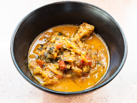 cooked Chakhokhbili (traditional georgian dish from stewed chicken, tomato, eggplant and fresh herbs) in black bowl in home kitchenの写真素材