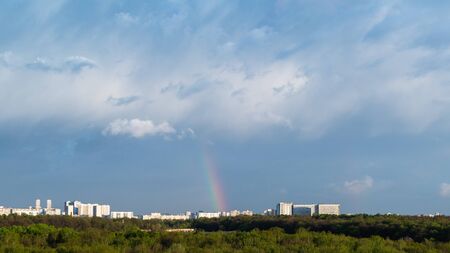 blue thunderclouds and rainbow over city on sunny spring dayの写真素材