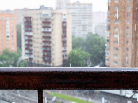 wet balcony railing and view of blurred residential district on background in heavy rain in Moscow city (focus on the railing)の写真素材