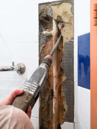 repairing of plumbing riser of heated towel rail at home - breaking wall to clean water pipe from concrete with rotary hammerの写真素材