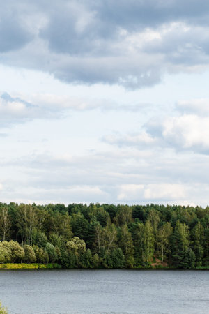 gray clouds in blue sky over green forest on coast of lake in September evening