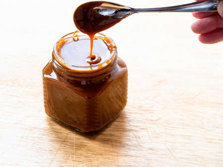 cooking salted butter caramel sauce at home kitchen - homemade smooth cooked salty caramel dessert in open glass jar on wooden boardの写真素材