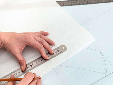 tailor's hands redraw pattern layout of dress with pencil and ruler on tracing-paper from graph...