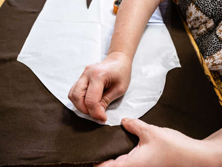 woman fixes paper pattern layout of dress to brown fabric by pin at homeの写真素材