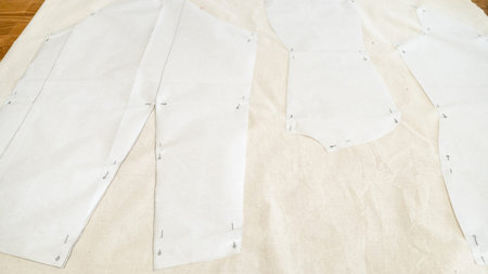 fixed paper pattern layouts of dress on calico fabric on wooden table at home