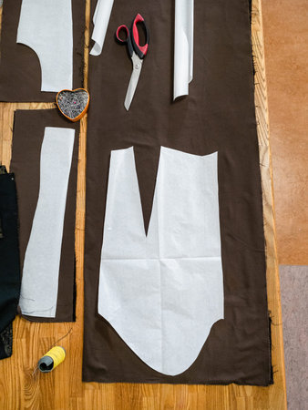top view of sartorial tools and patterns layouts of dress on brown fabric on wooden table at home