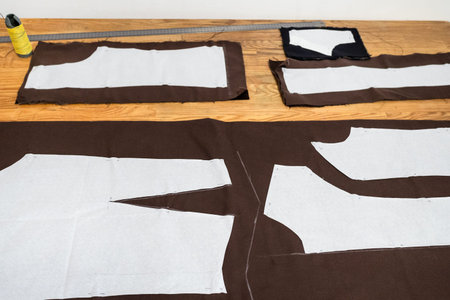 view of layouts of sewing patterns of dress on brown fabric on wooden table at home