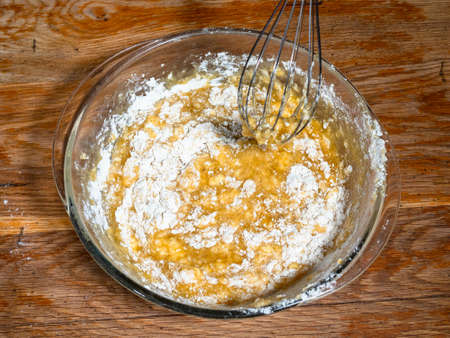 cooking sweet sponge cake at home - above view of mixing of dough from flour and sweet ingredients by whisk in glass bowl on old wooden table at home kitchenの写真素材