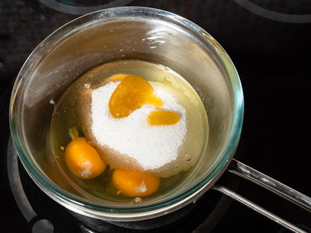cooking sweet sponge cake at home - above view of honey, sugar on raw eggs in glass bowl on water bath on stove at home kitchenの写真素材