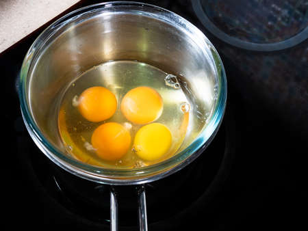 cooking sweet sponge cake at home - above view of four eggs in glass bowl on water bath on stove at home kitchenの写真素材