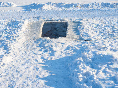 snowy footpat to large swimming ice-hole in in frozen pond on cold sunny winter dayの写真素材