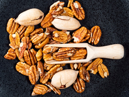 top view of wooden scoop on pecan nuts on black plate