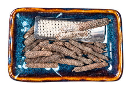 top view of java long pepper catkins and grater in ceramic bowl cutout on white background