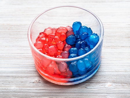red and blue colored boiled tapioca balls in glass bowl on gray wooden table