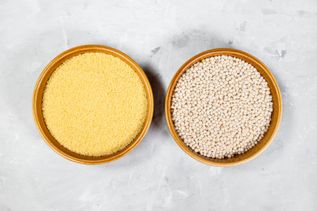 top view of Moroccan and Israeli couscous in round ceramic bowls on gray concrete board
