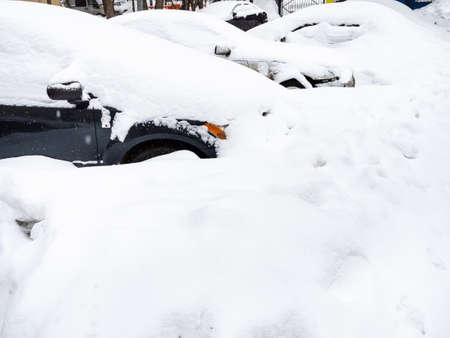 deep snowbanks cover parked cars on city street after snowfall on winter dayの写真素材