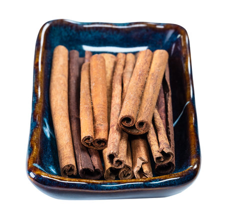end view of quills of cassia cinnamon in ceramic bowl cutout on white background