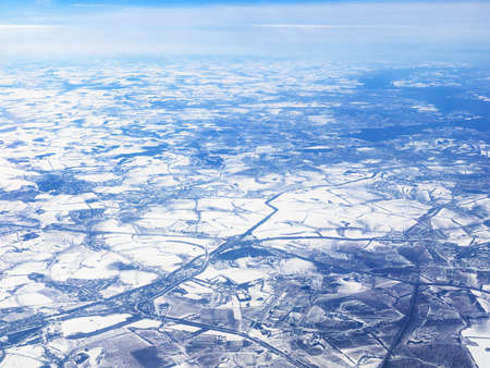aerial view of snow-covered earth from porthole while flying by planeの写真素材