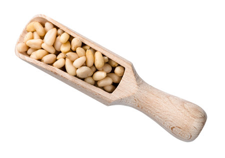 top view of peeled pine nuts in wooden scoop cutout on white background