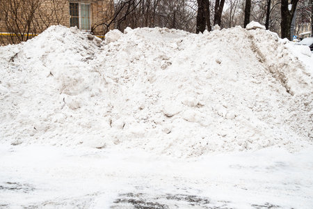 pile of snow removed from city road on lawn near residential building in Moscow city on winter dayの写真素材