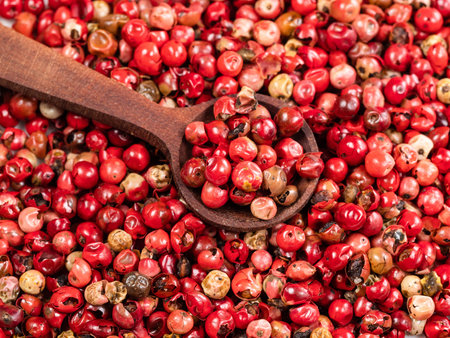 wooden spoon on pile of pink peppercorns (Baie rose) closeup