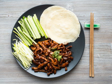 chinese cuisine - top view of pork in peking soy sauce with sliced scallion, cucumber and rice...