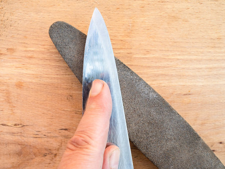 sharpening kitchen knife closeup on whetstone on wooden board
