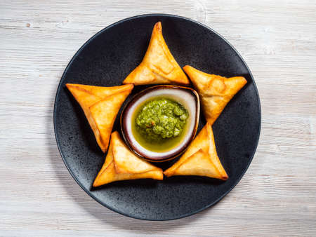 top view of Peruvian Empanadas (fried Turnover filled with meat) with green Chimichurri sauce on plate on wooden boardの写真素材