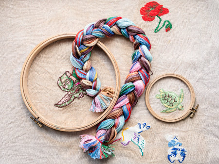top view of floss threads woven into braid and wooden hoops on fabric with embroideries