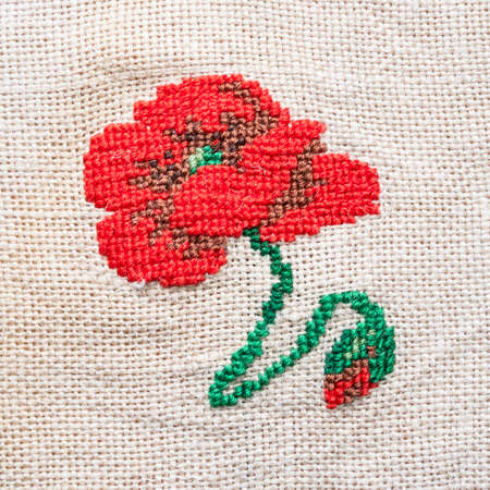 red poppy flower embroidered by hand on fabric close upの写真素材