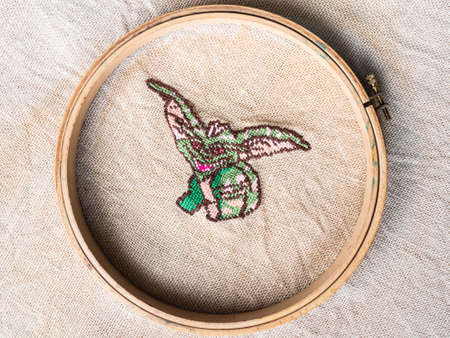 green gremlin in wooden hoop embroidered by hand on fabric close upの写真素材