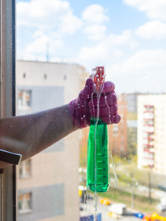 washing window in apartment in high-rise city house with spraying of washing liquid on surface of window glass on sunny spring dayの写真素材