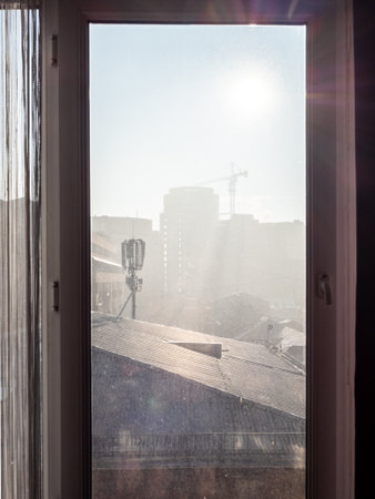 view through window glass of apartment on city houses in smog on sunny winter morningの写真素材