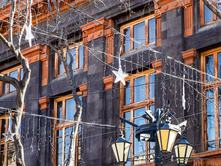 outdoor Christmas garlands and house covered with black Armenian tuff in background in Yerevan city on sunny winter dayの写真素材