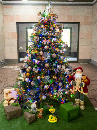 Christmas tree decorated with tinsel, garlands and balls with figure of Santa Claus and boxes with gifts in office hallの写真素材