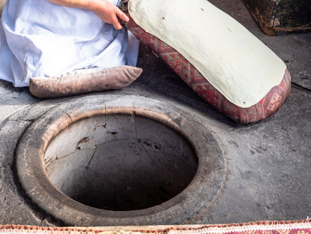 cooking of national dish of local cuisine Armenian lavash -baker prepares to place raw lavash dough into tandoor in courtyard of village houseの写真素材