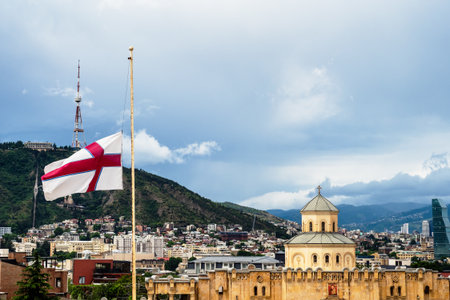 Georgian flag and skyline of Tbilisi city with Gate Church of Holy Trinity Cathedral (Sameba) of Tbilisi city on overcast summer day, Georgiaの写真素材