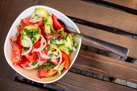top view of Georgian vegetable salad in white bowl on wooden table in outdoor local cafe in Borjomi town, Georgia on summer dayの写真素材