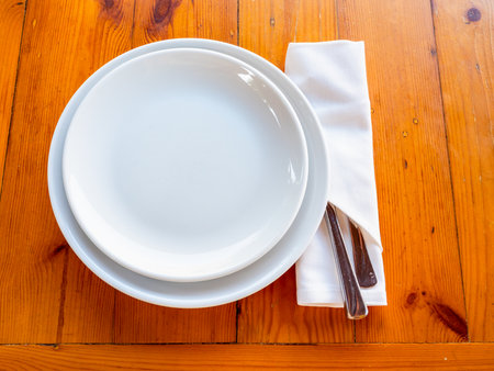above view of two empty white plates and knife and fork in napkin served on wooden tableの写真素材