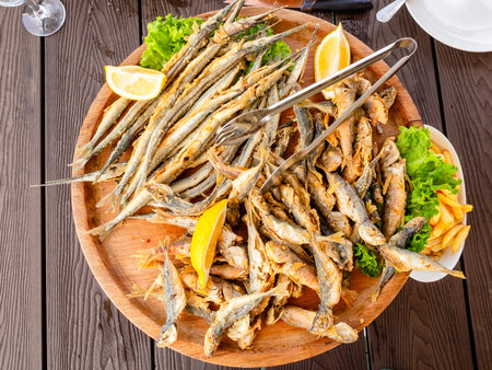 top view of wooden plate with various fried local Black Sea fishes on wooden table at outdoor fish market cafe in Batumi city, Georgiaの写真素材