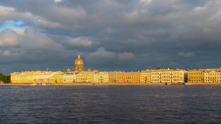 panoramic view of Embankment of Great Neva river with dome of Saint Isaac Cathedral in Saint Petersburg city, Russia lit by setting sun in sunny summer eveningの写真素材