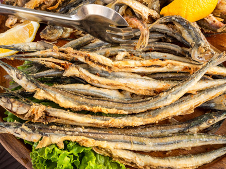 fried local Black Sea garfish fishes closeup on wooden plate at outdoor fish market cafe in Batumi city, Georgiaの写真素材