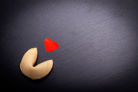 A fortune cookie with a little red heart on a black stone background. Are you ready to break the...